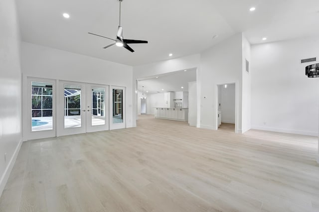 unfurnished living room with french doors, a towering ceiling, light hardwood / wood-style flooring, and ceiling fan