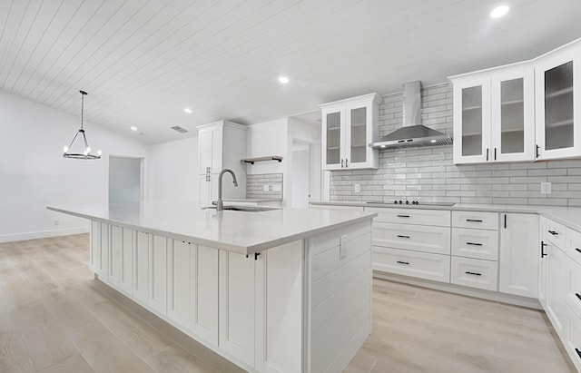 kitchen with white cabinets, hanging light fixtures, a kitchen island with sink, and wall chimney range hood