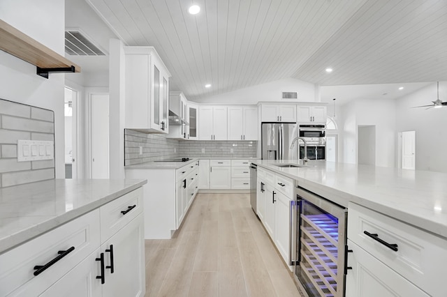 kitchen featuring white cabinets, appliances with stainless steel finishes, light stone countertops, and beverage cooler