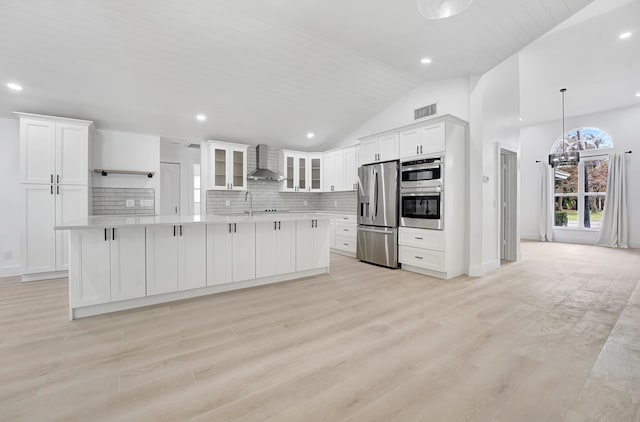 kitchen with white cabinetry, light hardwood / wood-style flooring, wall chimney range hood, and appliances with stainless steel finishes