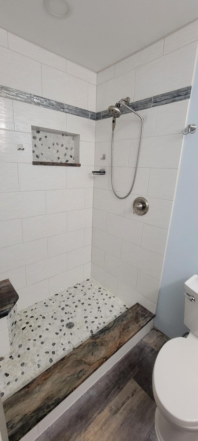 bathroom with toilet, hardwood / wood-style floors, and a tile shower