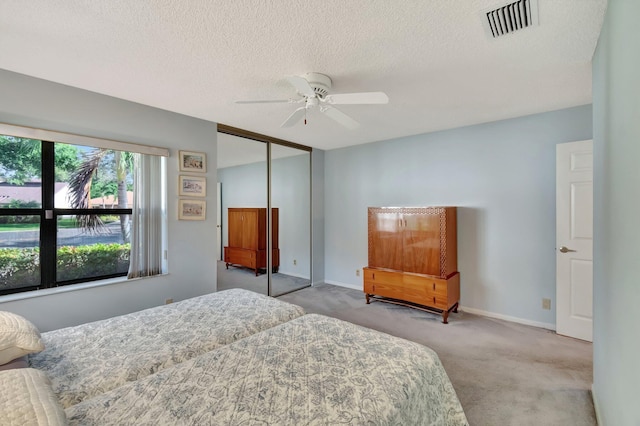 bedroom featuring a textured ceiling, a closet, ceiling fan, and light colored carpet