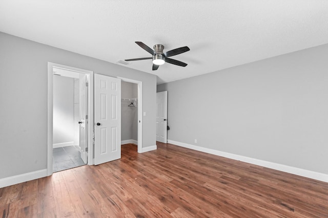 unfurnished bedroom with hardwood / wood-style floors, a walk in closet, ceiling fan, a textured ceiling, and a closet