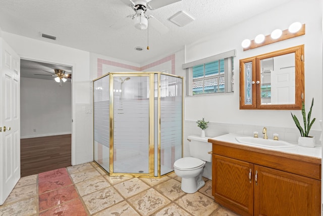 bathroom featuring vanity, a textured ceiling, a shower with door, ceiling fan, and toilet