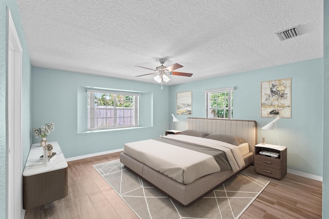 bedroom with a textured ceiling, light hardwood / wood-style floors, multiple windows, and ceiling fan