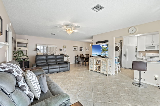 living room featuring light tile patterned floors, a textured ceiling, stacked washer and dryer, and ceiling fan