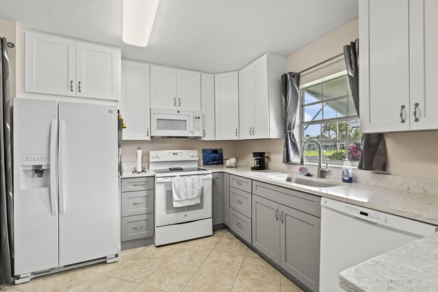 kitchen with light tile patterned flooring, white appliances, white cabinetry, and sink