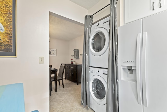 clothes washing area featuring a textured ceiling, light tile patterned floors, and stacked washer / dryer