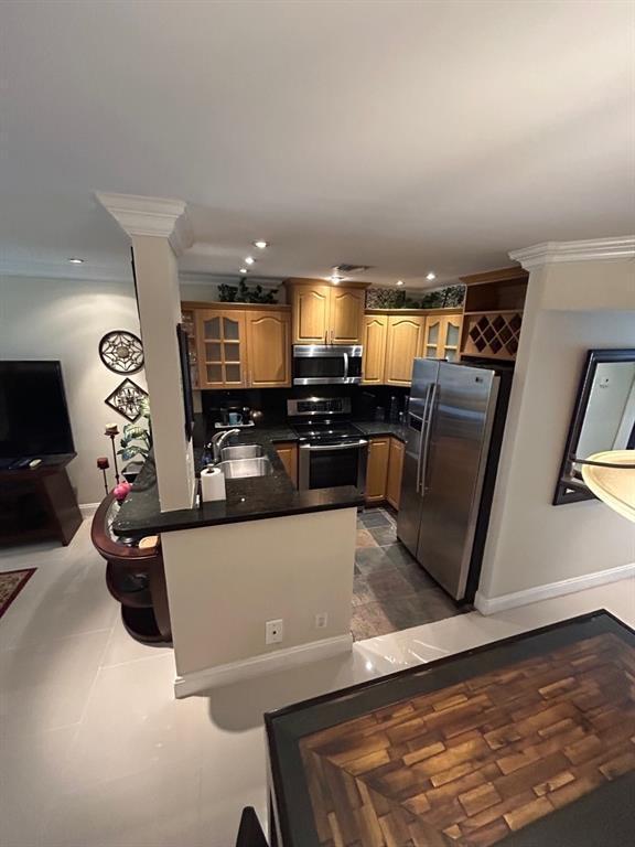 kitchen with sink, dark tile patterned floors, ornamental molding, appliances with stainless steel finishes, and kitchen peninsula