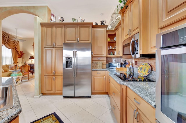 kitchen featuring dark stone countertops, light tile patterned floors, stainless steel appliances, and ornamental molding