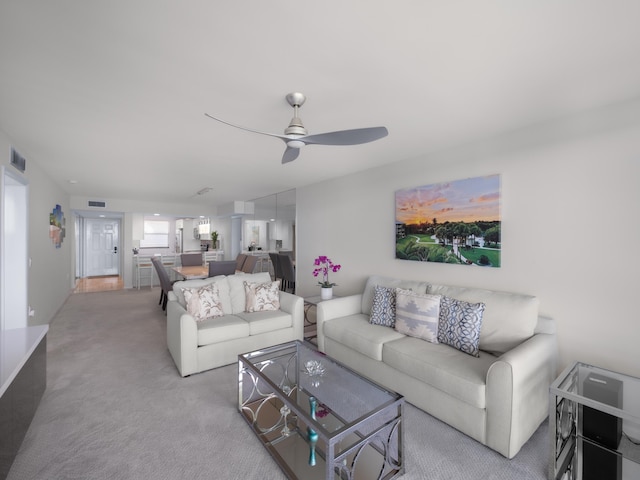 living area with a ceiling fan, visible vents, and light colored carpet