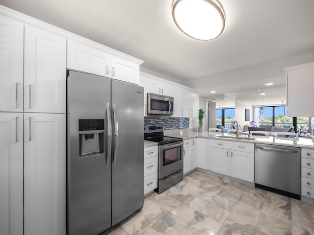 kitchen with tasteful backsplash, appliances with stainless steel finishes, marble finish floor, white cabinetry, and a sink