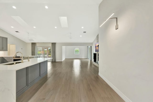 kitchen with gray cabinetry, vaulted ceiling with skylight, ceiling fan, light wood-type flooring, and a large island