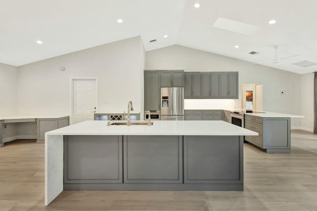 kitchen with gray cabinetry, stainless steel appliances, sink, a large island with sink, and light hardwood / wood-style floors