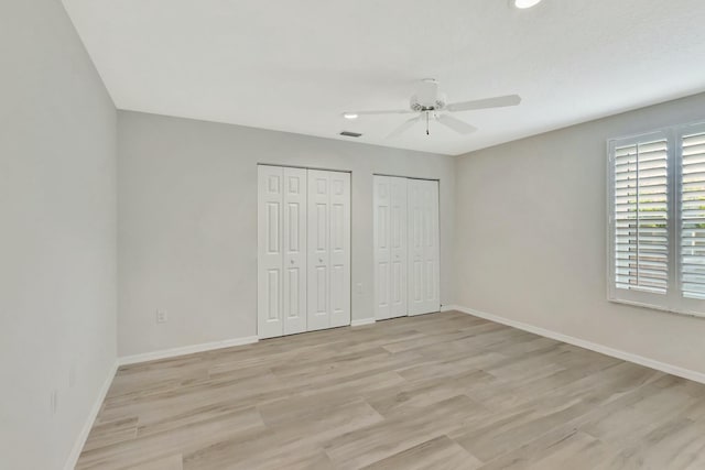 unfurnished bedroom with ceiling fan, light hardwood / wood-style floors, and two closets