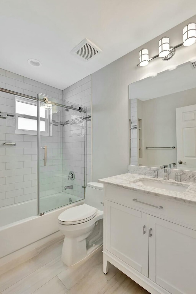 full bathroom with combined bath / shower with glass door, vanity, and toilet