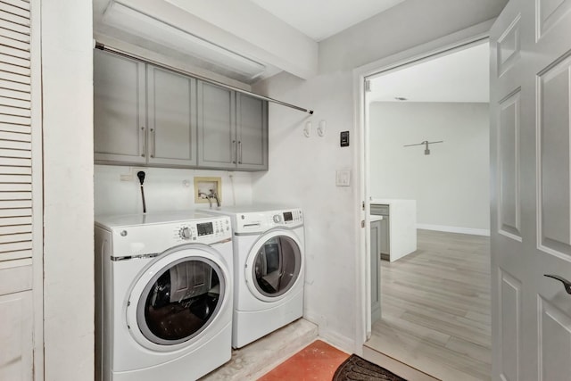 laundry area with washing machine and clothes dryer, cabinets, and light hardwood / wood-style floors