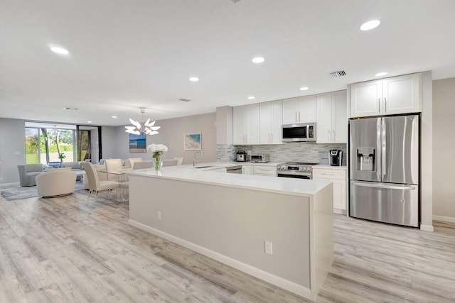 kitchen with kitchen peninsula, stainless steel appliances, hanging light fixtures, a chandelier, and white cabinets