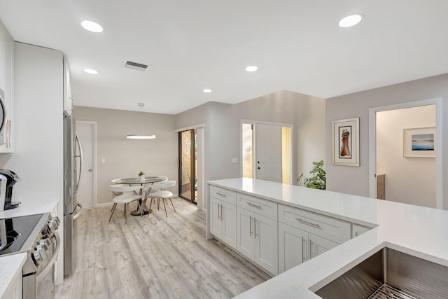 kitchen with white cabinets, appliances with stainless steel finishes, light wood-type flooring, and pendant lighting