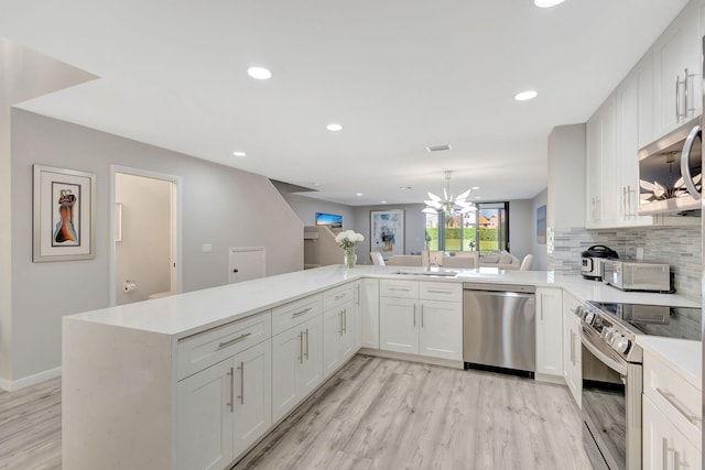 kitchen featuring kitchen peninsula, white cabinets, stainless steel appliances, and light wood-type flooring