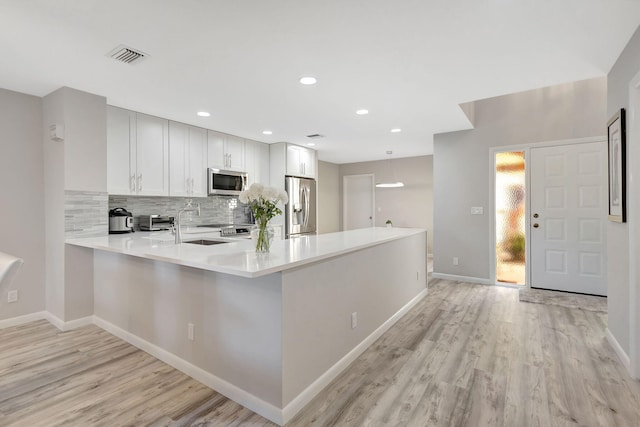 kitchen featuring backsplash, kitchen peninsula, light wood-type flooring, white cabinetry, and stainless steel appliances