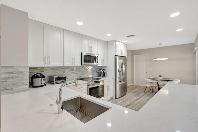 kitchen with white cabinets, sink, light wood-type flooring, decorative light fixtures, and stainless steel appliances