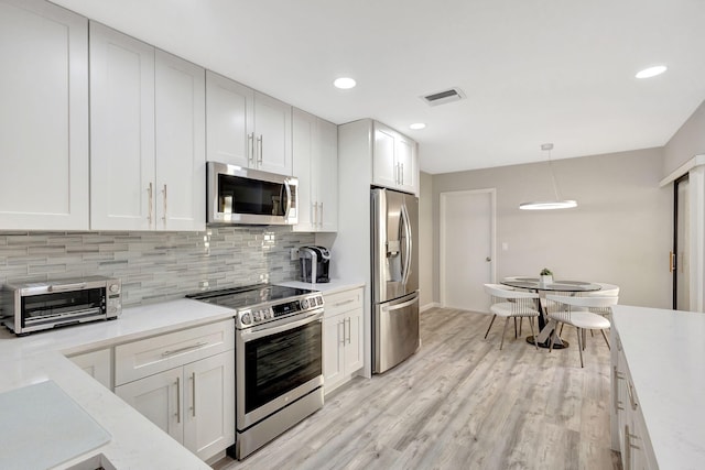 kitchen with white cabinets, decorative light fixtures, appliances with stainless steel finishes, and light hardwood / wood-style flooring