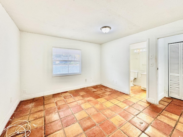 unfurnished bedroom featuring a closet, a textured ceiling, and ensuite bath