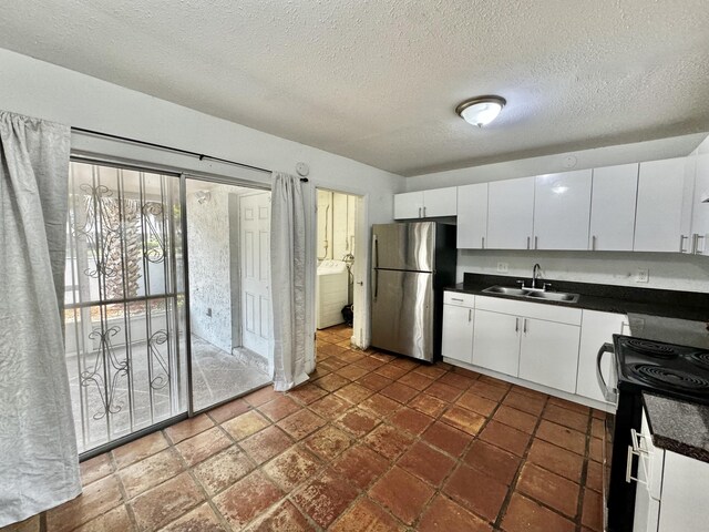 kitchen with dark countertops, electric range, freestanding refrigerator, white cabinets, and a sink