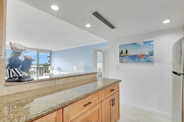 kitchen with light tile patterned floors, light brown cabinets, stainless steel refrigerator, and light stone counters