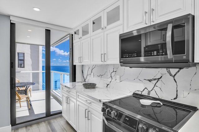 kitchen featuring decorative backsplash, appliances with stainless steel finishes, light stone countertops, white cabinets, and light hardwood / wood-style floors