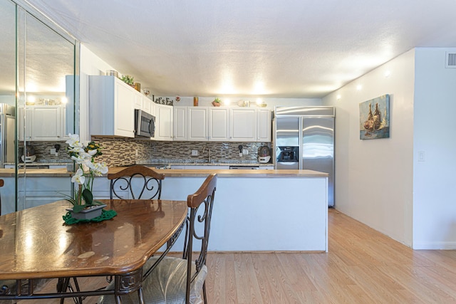 kitchen featuring light wood finished floors, tasteful backsplash, visible vents, white cabinets, and appliances with stainless steel finishes