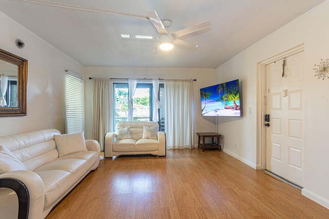 living area with light wood finished floors, a ceiling fan, and baseboards