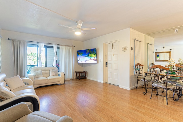 living area with light wood-style floors, baseboards, and a ceiling fan