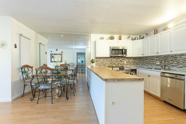 kitchen with white cabinets, appliances with stainless steel finishes, light wood-style floors, wooden counters, and backsplash