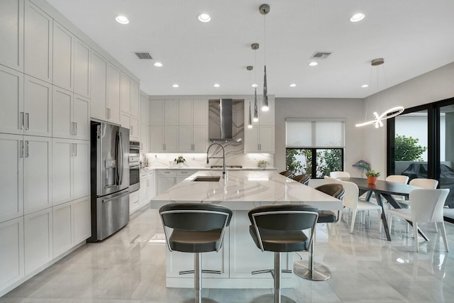 kitchen with light stone countertops, a large island with sink, wall chimney exhaust hood, stainless steel appliances, and tasteful backsplash