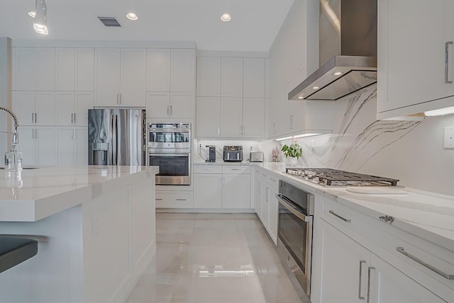 kitchen featuring white cabinetry, wall chimney range hood, appliances with stainless steel finishes, and decorative backsplash