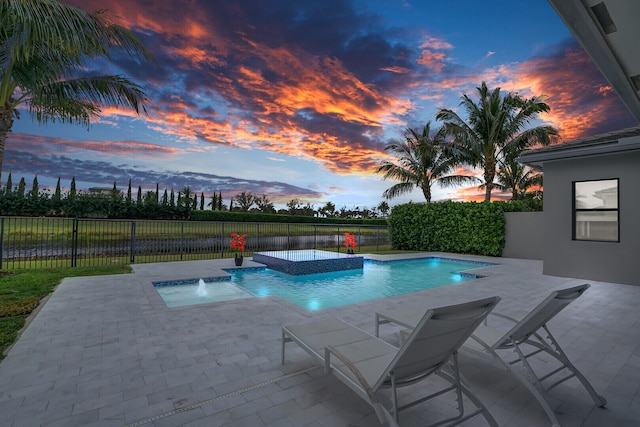 pool at dusk featuring pool water feature, a patio, and an in ground hot tub