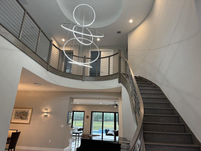 staircase with ceiling fan with notable chandelier, a tray ceiling, and a towering ceiling