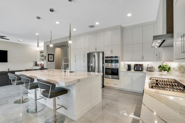 kitchen with a large island with sink, appliances with stainless steel finishes, decorative light fixtures, light stone counters, and a breakfast bar area