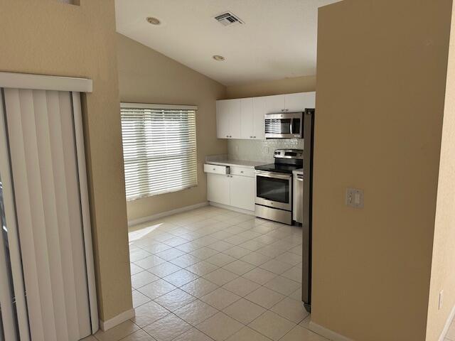 kitchen featuring backsplash, white cabinets, vaulted ceiling, light tile patterned floors, and stainless steel appliances