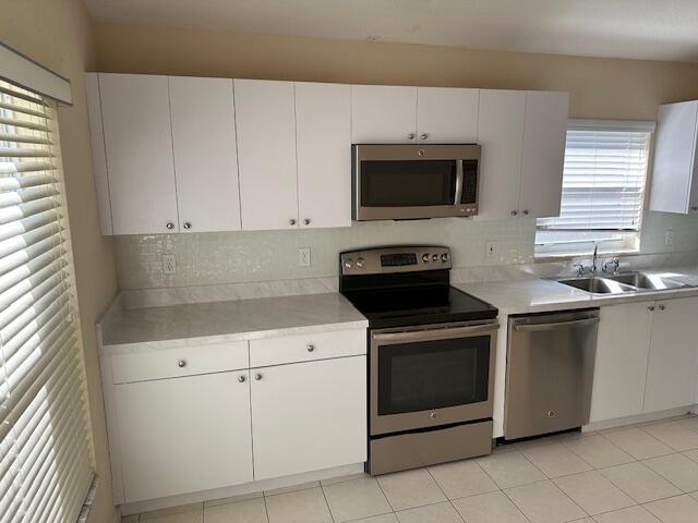 kitchen featuring tasteful backsplash, stainless steel appliances, sink, light tile patterned floors, and white cabinetry