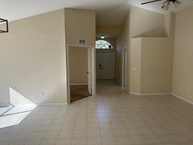 empty room with ceiling fan, high vaulted ceiling, and light tile patterned floors