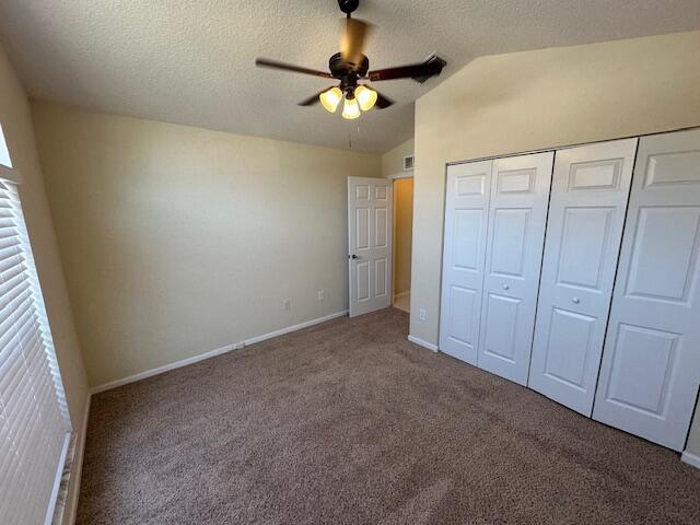 unfurnished bedroom featuring ceiling fan, a closet, carpet floors, and vaulted ceiling