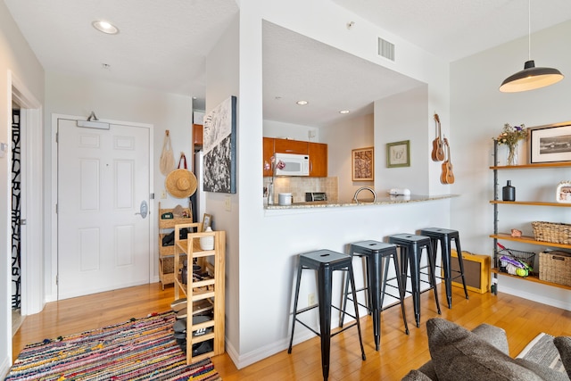 kitchen with light stone countertops, light wood-type flooring, kitchen peninsula, and tasteful backsplash