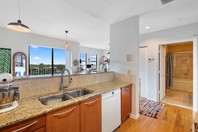 kitchen with light stone counters, sink, decorative light fixtures, dishwasher, and light hardwood / wood-style floors