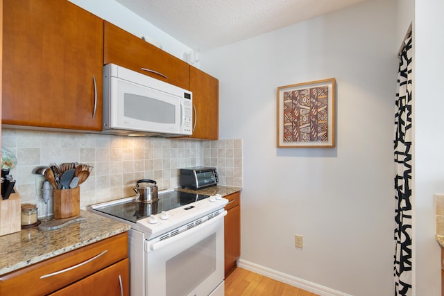 kitchen featuring light stone countertops, tasteful backsplash, light hardwood / wood-style flooring, a textured ceiling, and white appliances