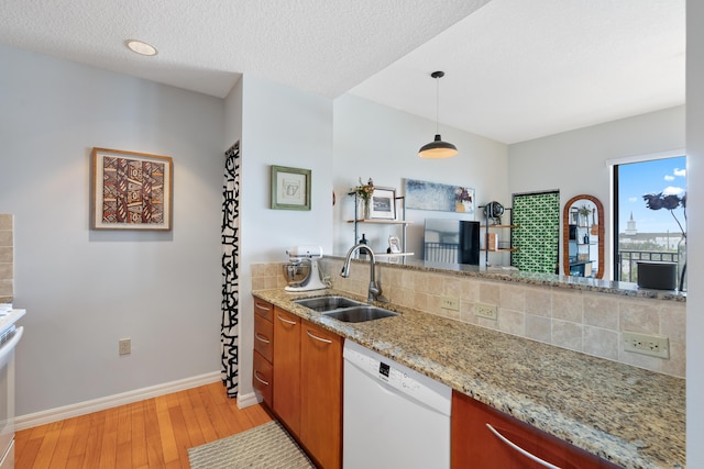 kitchen featuring dishwasher, sink, hanging light fixtures, light stone counters, and light wood-type flooring