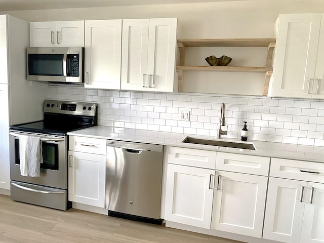 kitchen featuring backsplash, sink, light wood-type flooring, appliances with stainless steel finishes, and white cabinetry