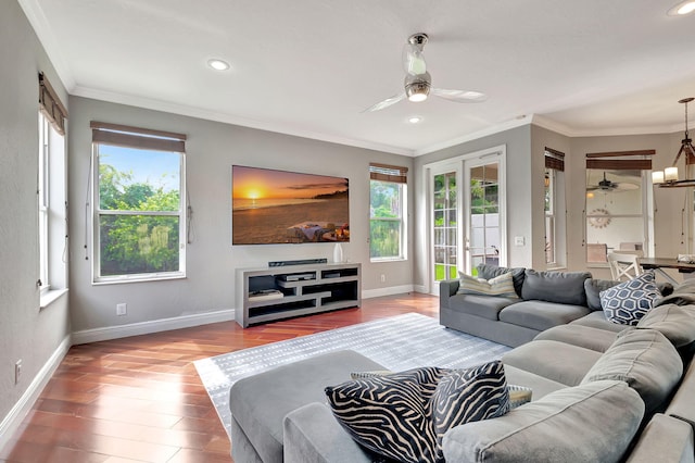 living room featuring ceiling fan with notable chandelier, a healthy amount of sunlight, wood-type flooring, and ornamental molding